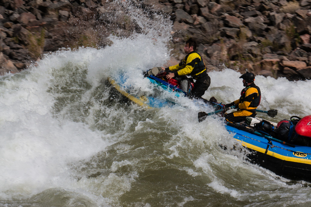 Group of people in a river raft going over rapids being sprayed with water